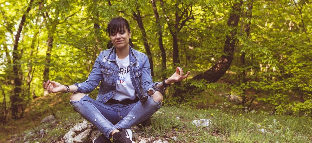 A woman meditates peacefully in a lush green forest, exuding calm and relaxation.