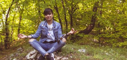 A woman meditates peacefully in a lush green forest, exuding calm and relaxation.