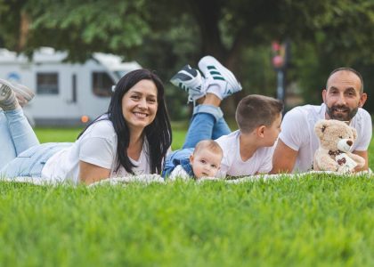 Happy family lying on grass with RV in the background, enjoying a sunny outdoor picnic.