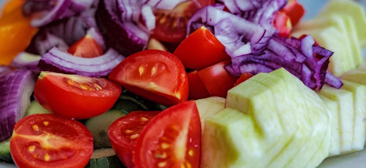 Colorful summer vegetable salad featuring tomatoes, cucumbers, and red onion slices on a plate.