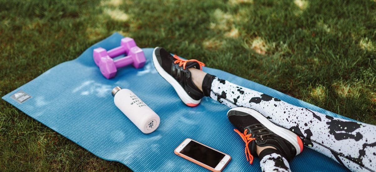 Focused workout setup outdoors with mat, dumbbells, phone, and water bottle.