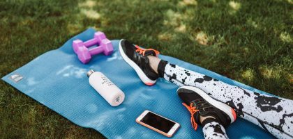 Focused workout setup outdoors with mat, dumbbells, phone, and water bottle.