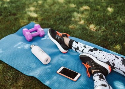 Focused workout setup outdoors with mat, dumbbells, phone, and water bottle.